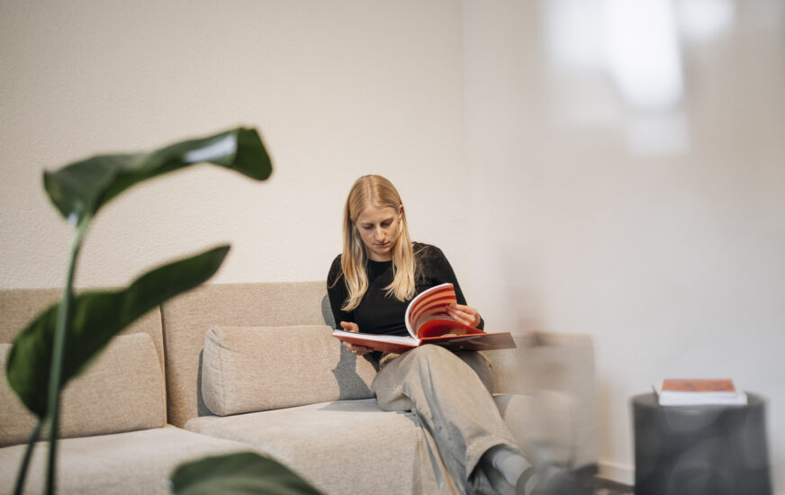 Bueroparallel - Mitarbeiterin auf dem Sofa mit Zeitschrift